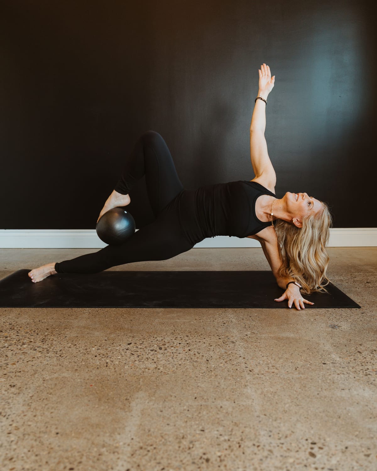A teacher in a side-plank balance with a Pilates ball