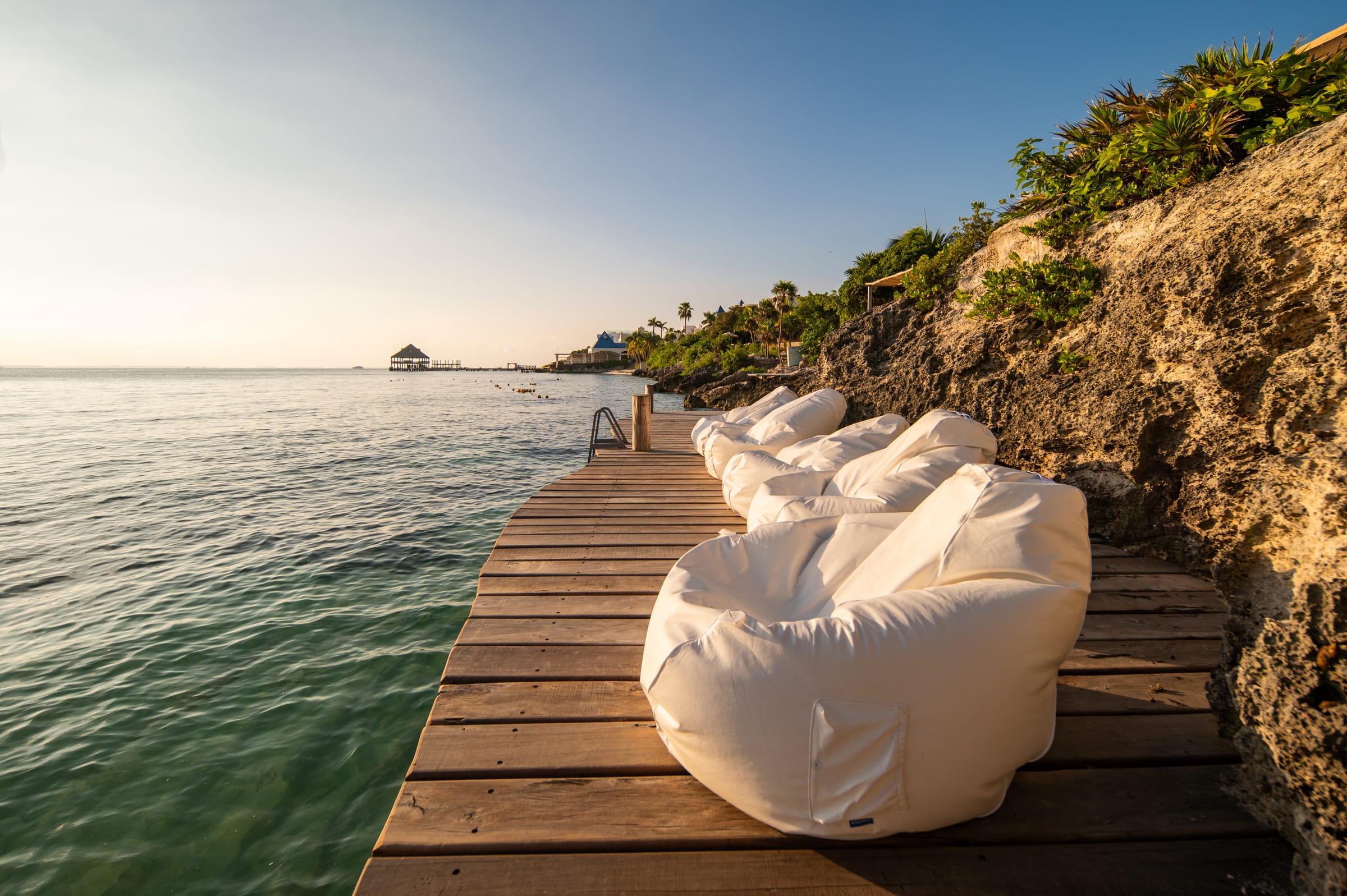 Loungers on the wooden sea deck at Casa Coco, looking down the coastline at golden hour