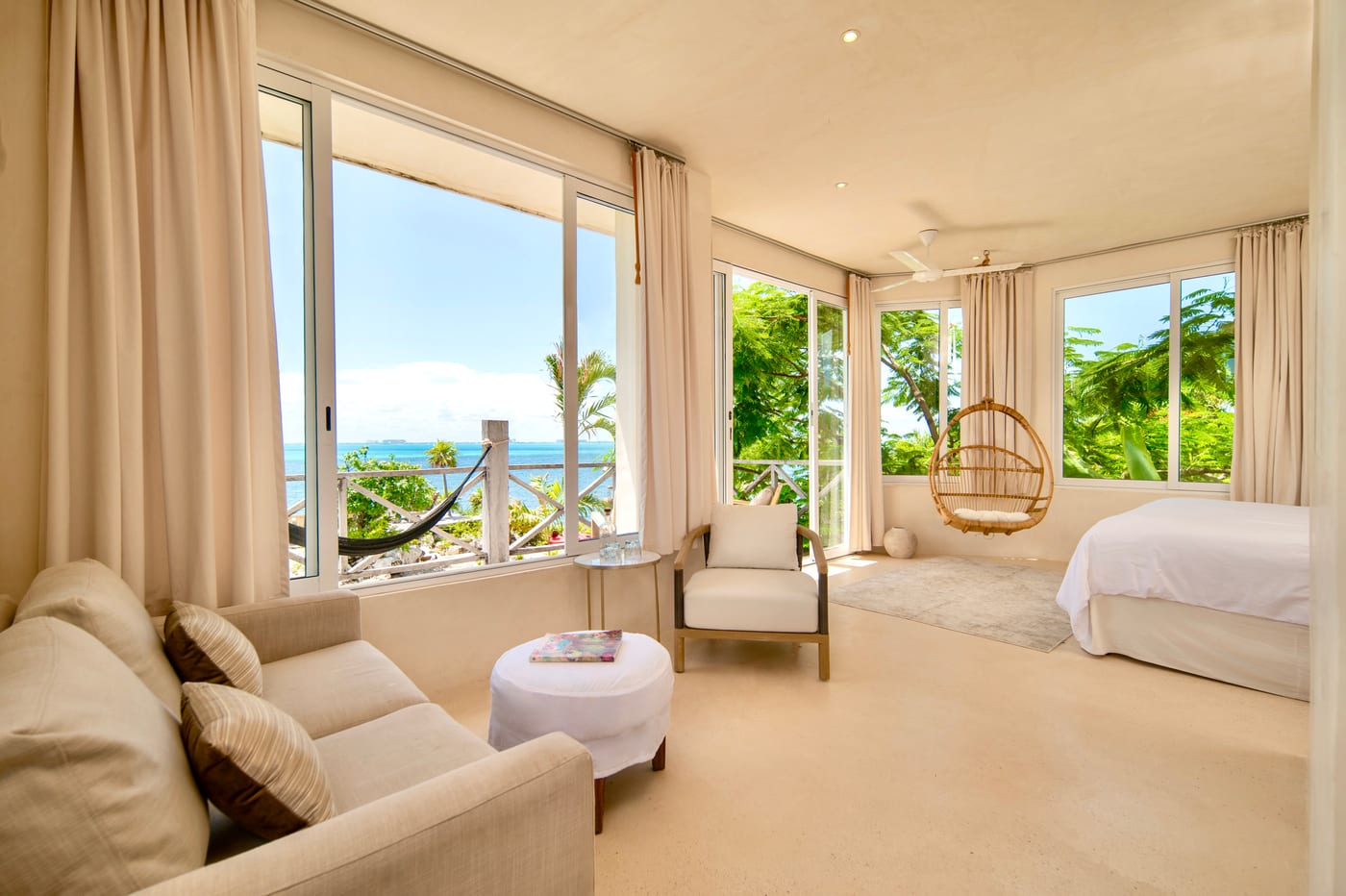 Premium corner room with king bed, sitting area and hanging chair, walls of windows opening to Caribbean views