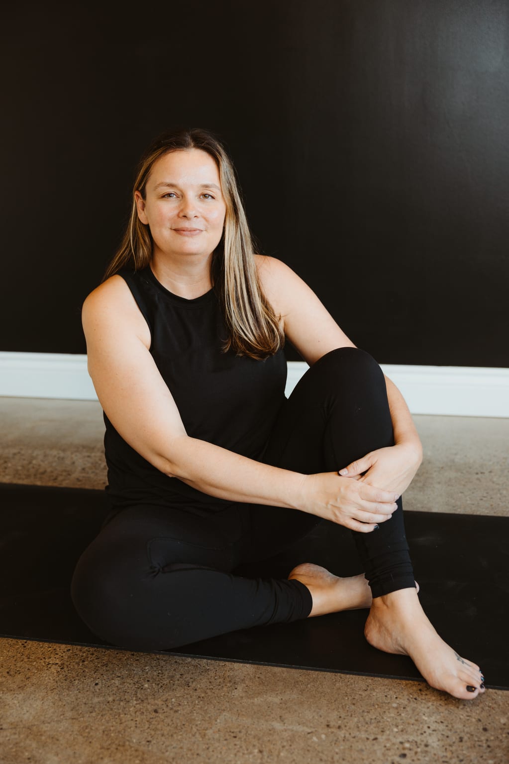 A Lineage teacher seated on her mat against the studio wall